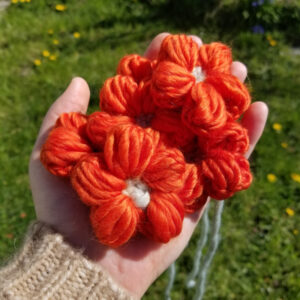 A pile of orange-red puff stitch crochet flowers held in a hand
