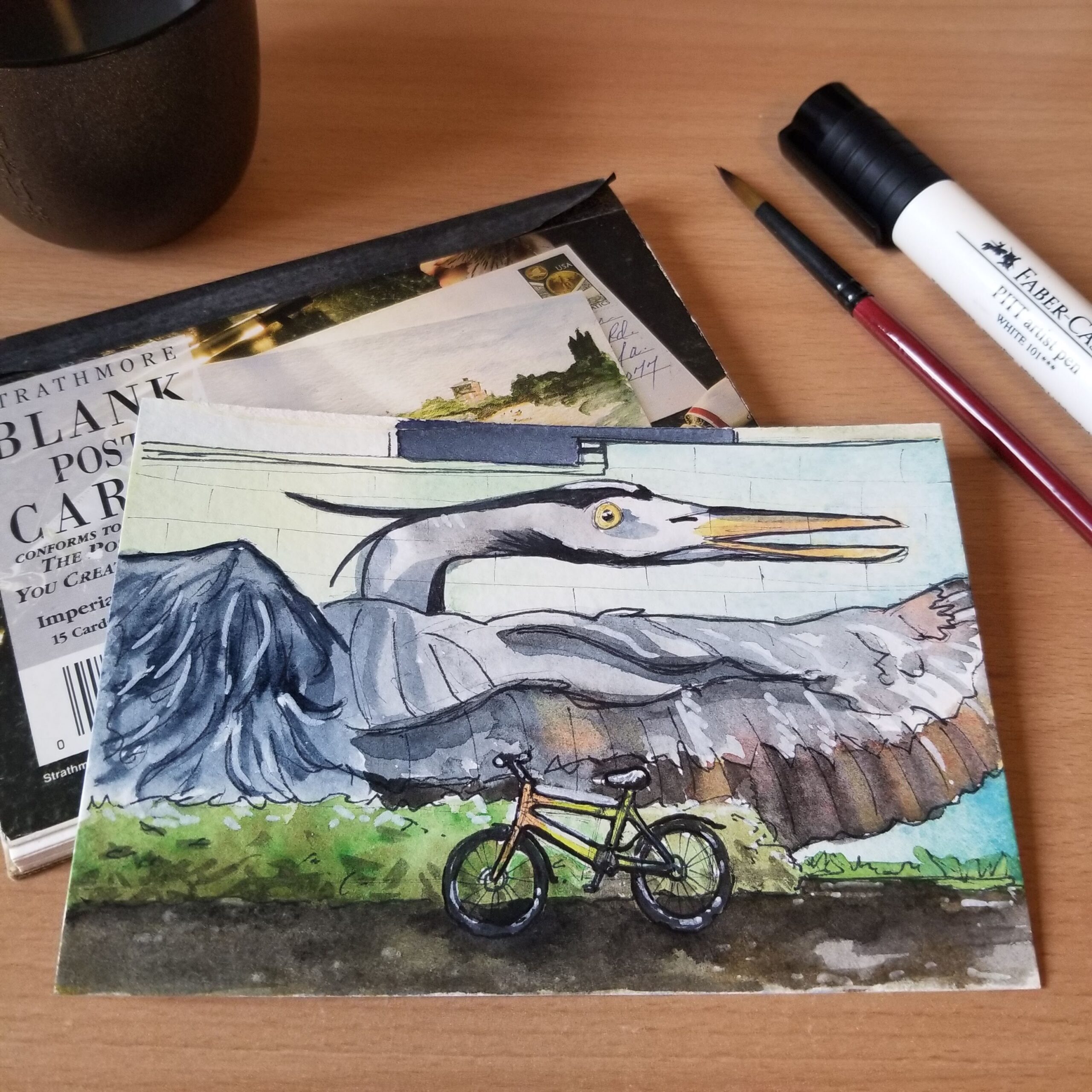 Watercolor postcard featuring a multi-colored commuter bike in front of a blue heron mural.