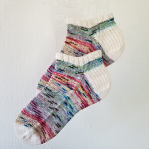 Hand knit ankle socks in variegated colors with white trim against a white background