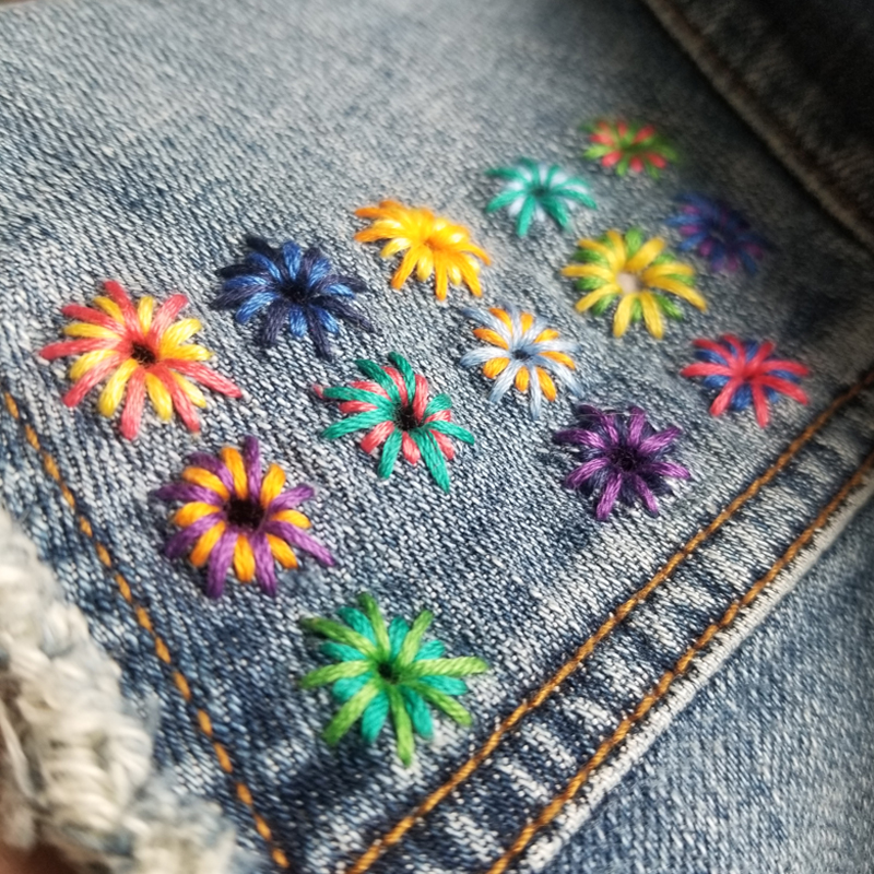 Brightly colored embroidered starbursts mend holes on a denim vest