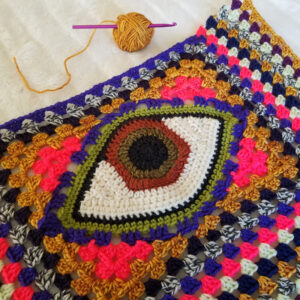 A crochet eye motif surrounded by granny square crochet in a number of psychedelic colors
