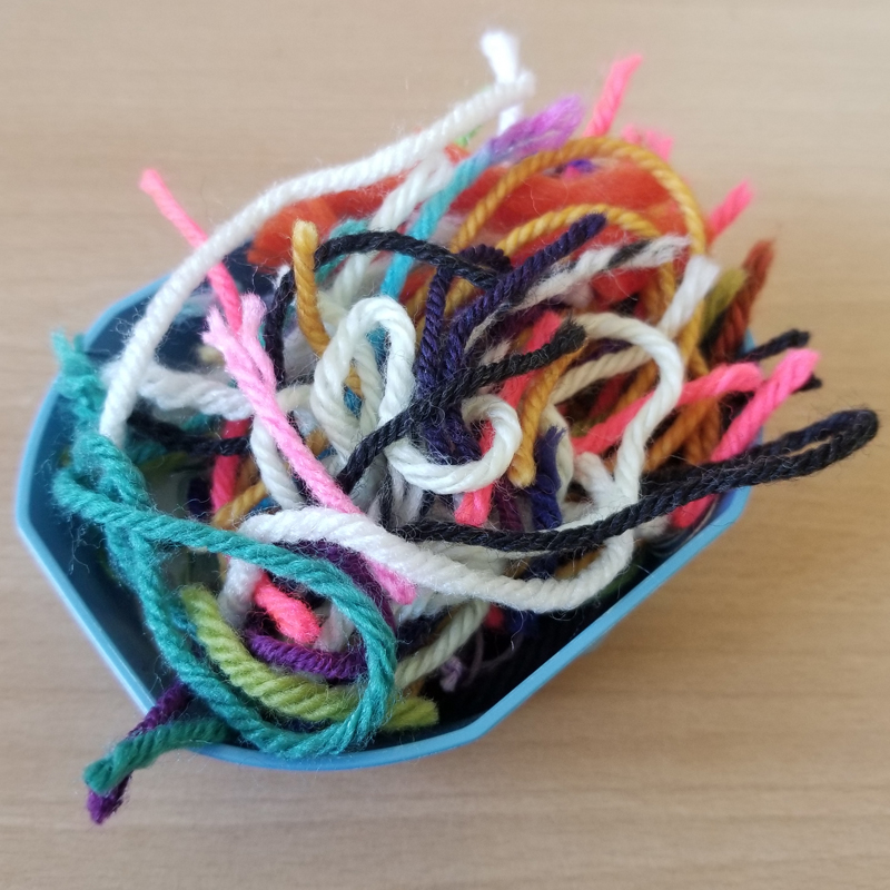 Multicolored scraps of yarn in a small blue octagonal plastic dish.