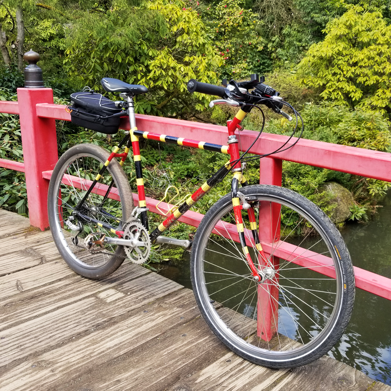 An 80's mountain bike turned commuter bike painted like a coral snake rests against the rail of a Japanese-style bridge.
