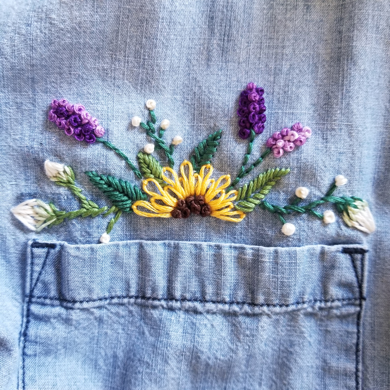 Embroidered sunflower, lavender, and white buds on a chambray shirt just above the pocket