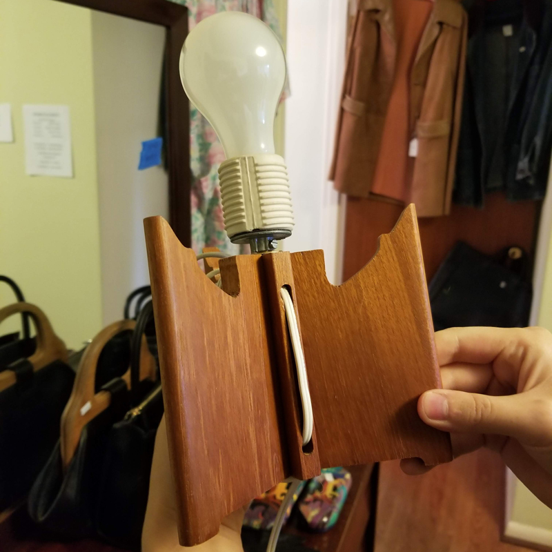 A hand holds up a teak mid century modern lamp base with a light bulb