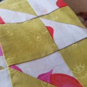Closeup picture of a fabric bag quilted in yellow ochre and white with pink fabrics in the Amish Star pattern